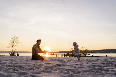 Deutschland, Bayern, Herrsching, Vater und Tochter spielen bei Sonnenuntergang am Strand - DIGF06761