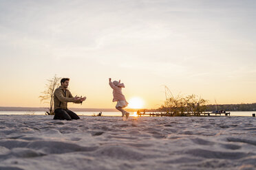 Deutschland, Bayern, Herrsching, Vater und Tochter spielen bei Sonnenuntergang am Strand - DIGF06762