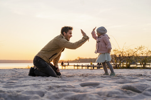 Deutschland, Bayern, Herrsching, Vater und Tochter spielen bei Sonnenuntergang am Strand, lizenzfreies Stockfoto