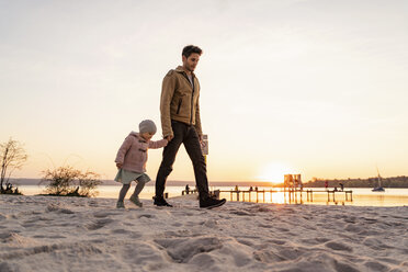 Germany, Bavaria, Herrsching, father and daughter walking on the beach at sunset - DIGF06765