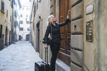 Italien, Florenz, reife, schwarz gekleidete Frau mit Rollkoffer vor Eingangstür stehend - FBAF00387