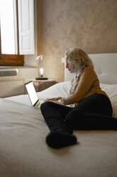 Reife Geschäftsfrau liegt auf dem Bett und arbeitet am Laptop - FBAF00395