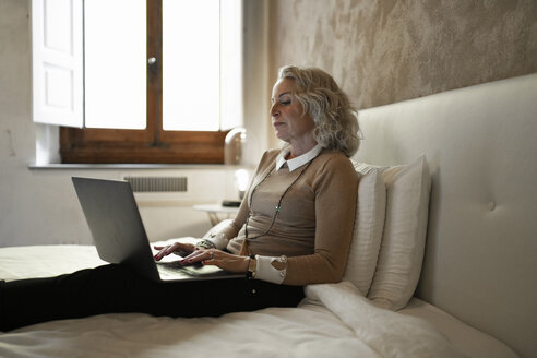 Mature businesswoman sitting on bed working on laptop - FBAF00404