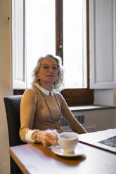 Portrait of content mature businesswoman sitting at table with laptop and cup of coffee - FBAF00432