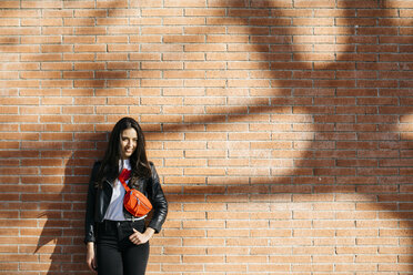 Young woman with a red bag resting on a brick wall - JRFF03081