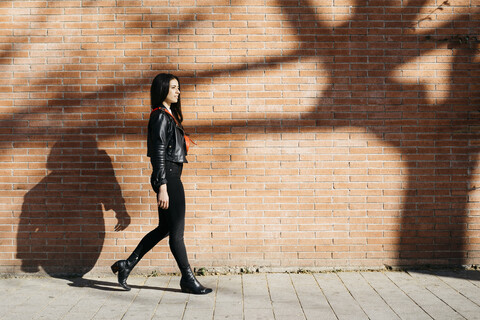 Junge Frau mit roter Tasche vor einer Backsteinmauer und einem Schatten eines Baumes, lizenzfreies Stockfoto