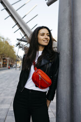 Happy young woman with a red hip bag in the city - JRFF03085