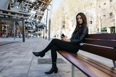 Junge Frau sitzt auf einer Bank und hält ihr Smartphone - JRFF03086