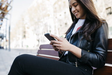 Junge Frau sitzt auf einer Bank und benutzt ein Smartphone - JRFF03089