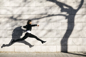 Young woman making a big jump on a wall with a shadow of a tree - JRFF03093