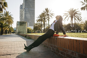 Young woman sitting on a wall, enjoying sunlight - JRFF03101