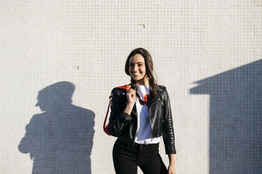 Happy young woman with a red hip bag, wall in the background - JRFF03106