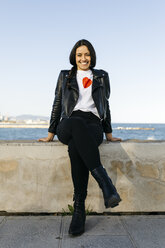 Young woman sitting on a wall, sea in the background - JRFF03111