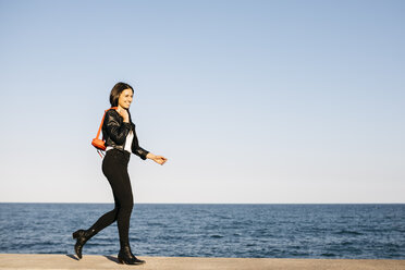 Glückliche Frau mit roter Tasche beim Spaziergang, das Meer im Hintergrund - JRFF03128
