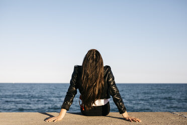 Junge Frau sitzt auf einer Mauer, im Hintergrund das Meer - JRFF03129