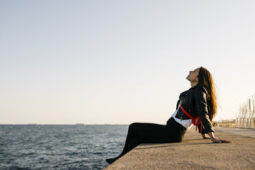 Young woman sitting on the floor at harbour - JRFF03130