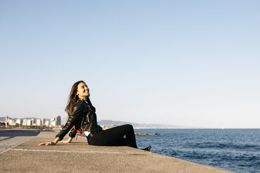 Young woman sitting on the wall at harbour - JRFF03131