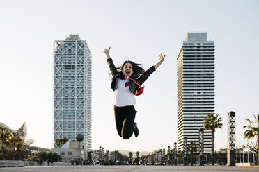 Spain, Barcelona, Young woman jumping, high-rise buildings in the background - JRFF03134