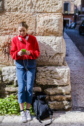 Junge Frau mit rotem Pullover, die in Verona ihr Smartphone benutzt - GIOF06294