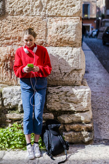 Junge Frau mit rotem Pullover, die in Verona ihr Smartphone benutzt - GIOF06294