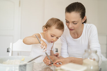 Mutter und kleine Tochter backen zusammen einen Kuchen in der Küche zu Hause - DIGF06772