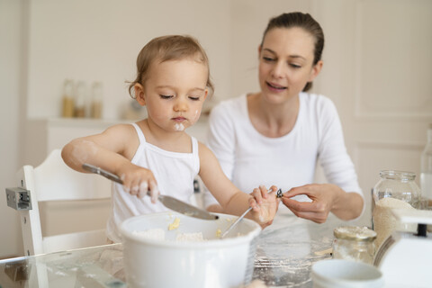 Mutter und kleine Tochter backen zusammen einen Kuchen in der Küche zu Hause, lizenzfreies Stockfoto