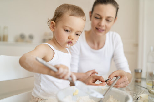 Mutter und kleine Tochter backen zusammen einen Kuchen in der Küche zu Hause - DIGF06774