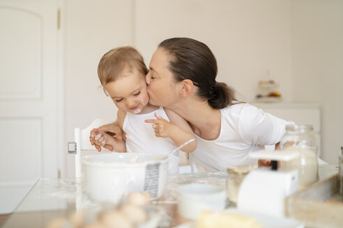 Mutter, die ihre kleine Tochter küsst, während sie in der Küche zu Hause einen Kuchen backt - DIGF06776