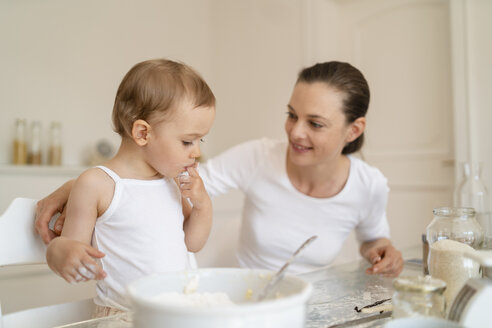 Mutter und kleine Tochter backen zusammen einen Kuchen in der Küche zu Hause - DIGF06777