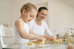 Mother and little daughter with dough roll making a cake together in kitchen at home - DIGF06783