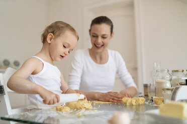 Mother and little daughter with dough roll making a cake together in kitchen at home - DIGF06784