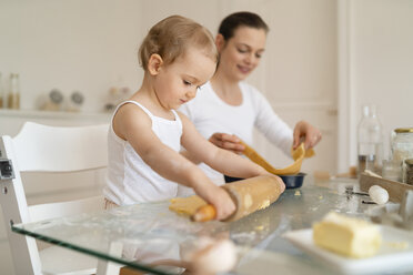 Mother and little daughter with dough roll making a cake together in kitchen at home - DIGF06786