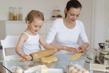 Mother and little daughter with dough roll making a cake together in kitchen at home - DIGF06787