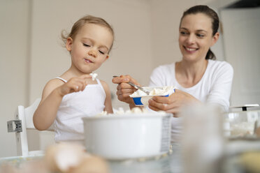 Mutter und kleine Tochter backen zusammen einen Kuchen in der Küche zu Hause - DIGF06792