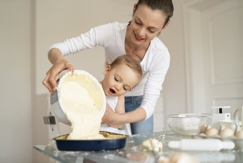 Mutter und kleine Tochter backen gemeinsam einen Kuchen und gießen Teig in eine Backform - DIGF06795