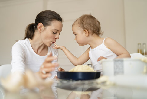 Kleines Mädchen, das seine Mutter füttert, während es einen Kuchen in der Küche zu Hause backt - DIGF06797