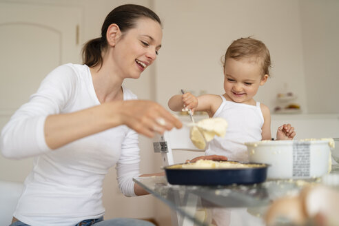 Glückliche Mutter und kleine Tochter machen einen Kuchen zusammen in der Küche zu Hause - DIGF06799