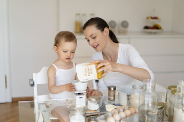 Mutter und kleine Tochter backen zusammen einen Kuchen in der Küche zu Hause und wiegen Mehl - DIGF06802