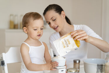 Mother and little daughter making a cake together in kitchen at home weighing flour - DIGF06803