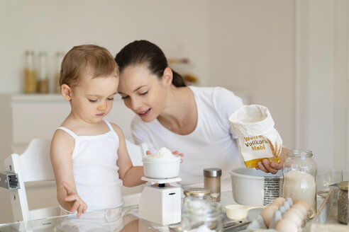 Mutter und kleine Tochter backen zusammen einen Kuchen in der Küche zu Hause und wiegen Mehl - DIGF06804