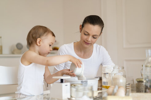 Mutter und kleine Tochter backen zusammen einen Kuchen in der Küche zu Hause - DIGF06805