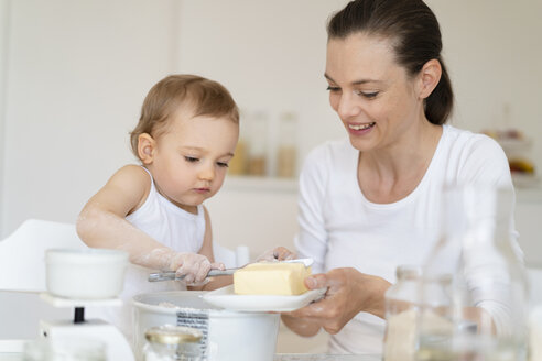 Mutter und kleine Tochter backen zusammen einen Kuchen in der Küche zu Hause - DIGF06810