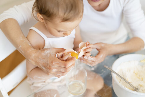 Mother and little daughter making a cake together in kitchen at home cracking an egg - DIGF06814