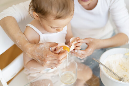 Mutter und kleine Tochter backen zusammen einen Kuchen in der Küche zu Hause und schlagen ein Ei auf - DIGF06814