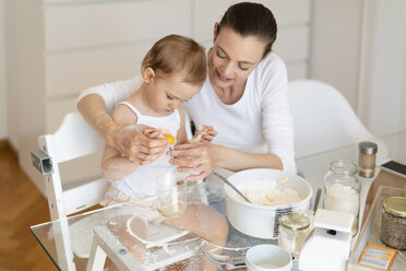 Mutter und kleine Tochter backen zusammen einen Kuchen in der Küche zu Hause - DIGF06815