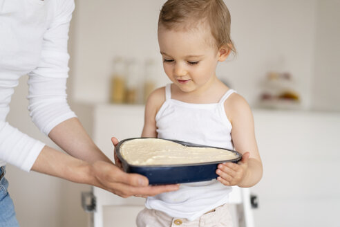 Kleines Mädchen und Mutter halten gemeinsam eine Backform mit Kuchenteig in der Küche zu Hause - DIGF06818