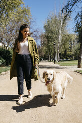 Happy woman going walkies in city park with her Labrador Retriever - JRFF03142
