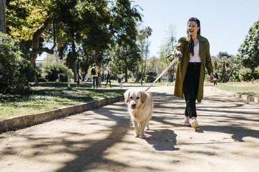 Happy woman going walkies in city park with her Labrador Retriever - JRFF03143