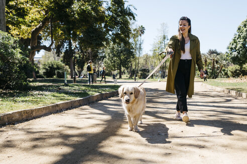 Glückliche Frau geht im Stadtpark mit ihrem Labrador Retriever spazieren - JRFF03143