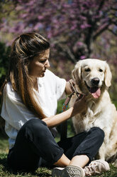 Woman and Labrador Retriever sitting on meadow in city park - JRFF03151